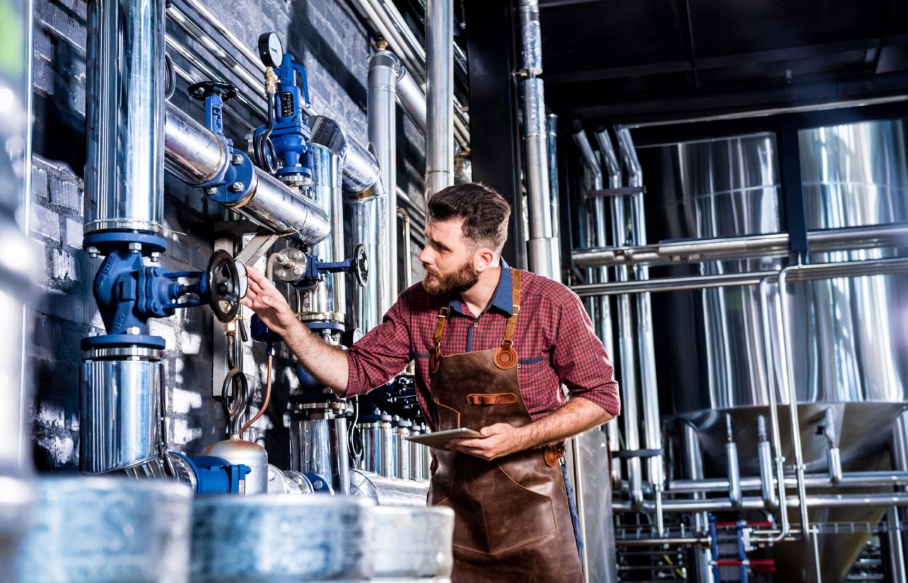 Brewer inspecting equipment using Edge analytics during beer brewing production holding iPad